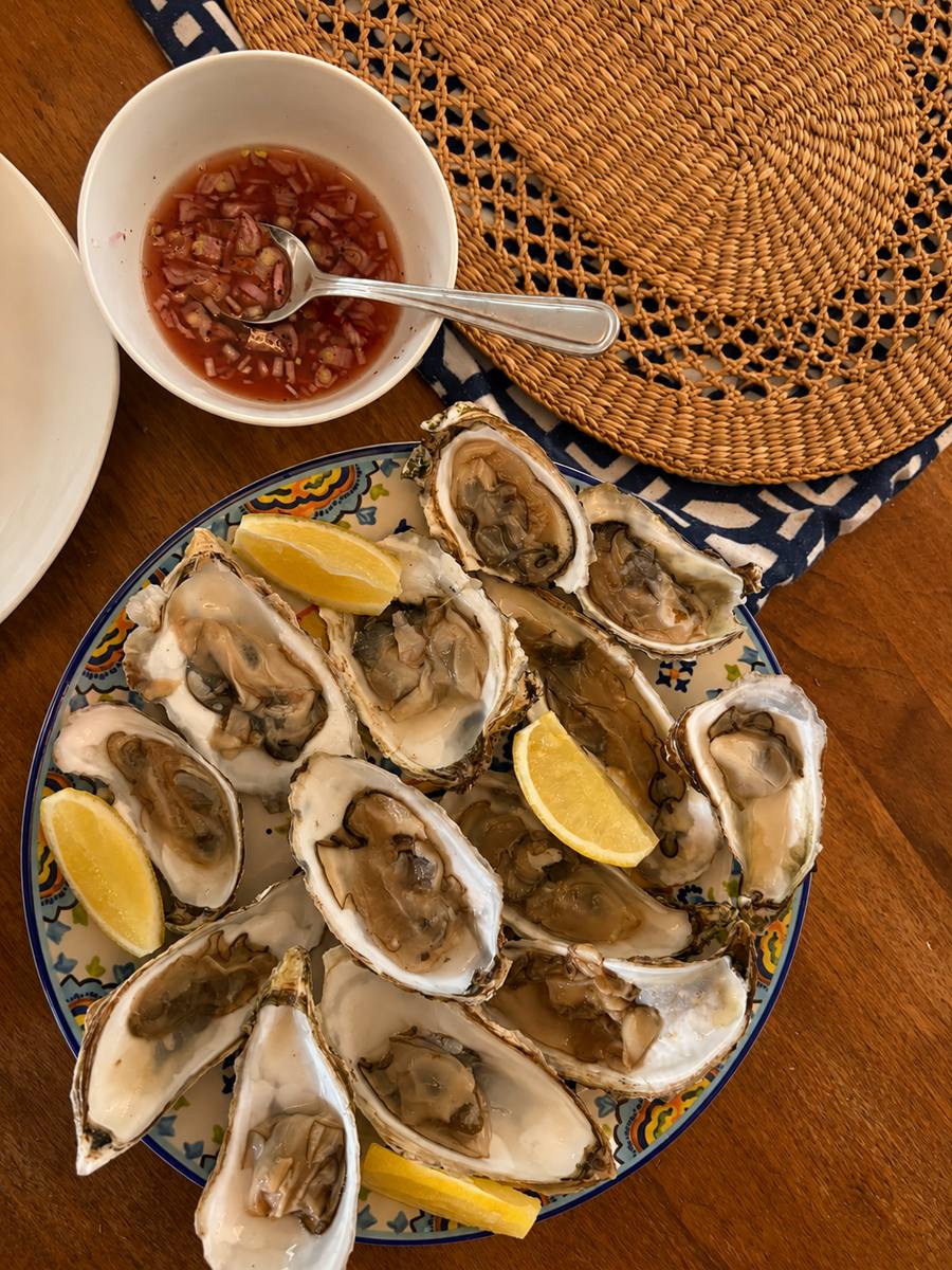A platter of oysters with lemon and a bowl of mignonette