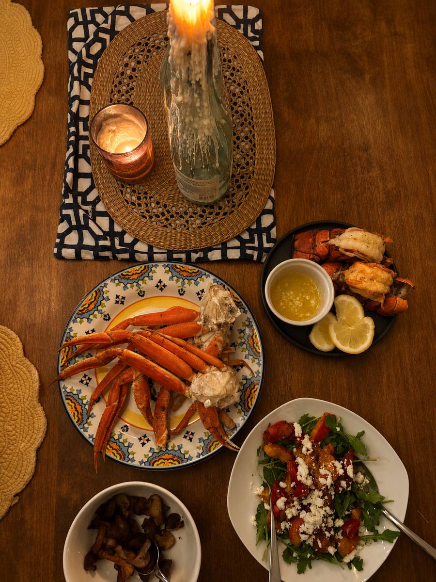 A candlelit dinner of crab legs, lobster tails, and salad on a wooden table