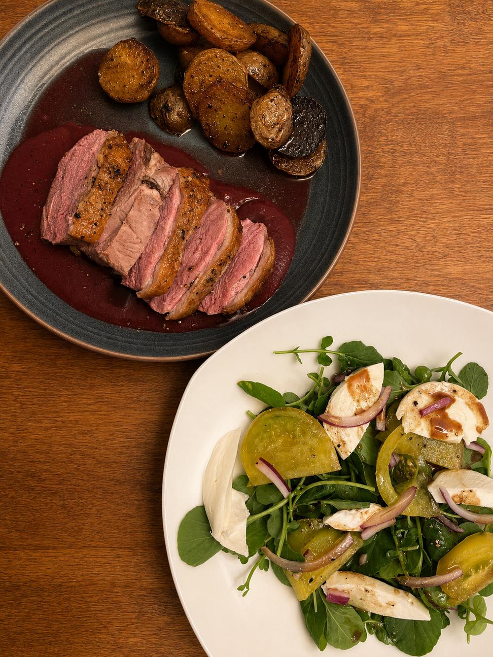 Sliced duck breast in a pool of blackberry balsamic sauce with crispy potatoes and a green salad