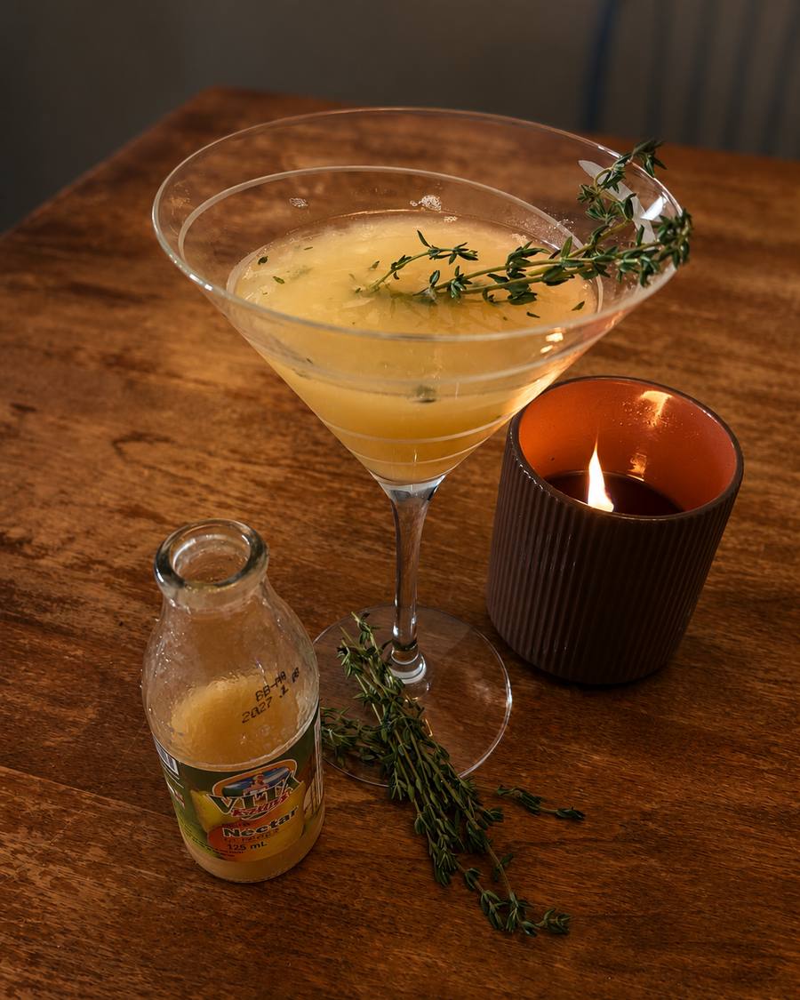 A pear and thyme martini beside a lit candle and a small bottle of pear nectar