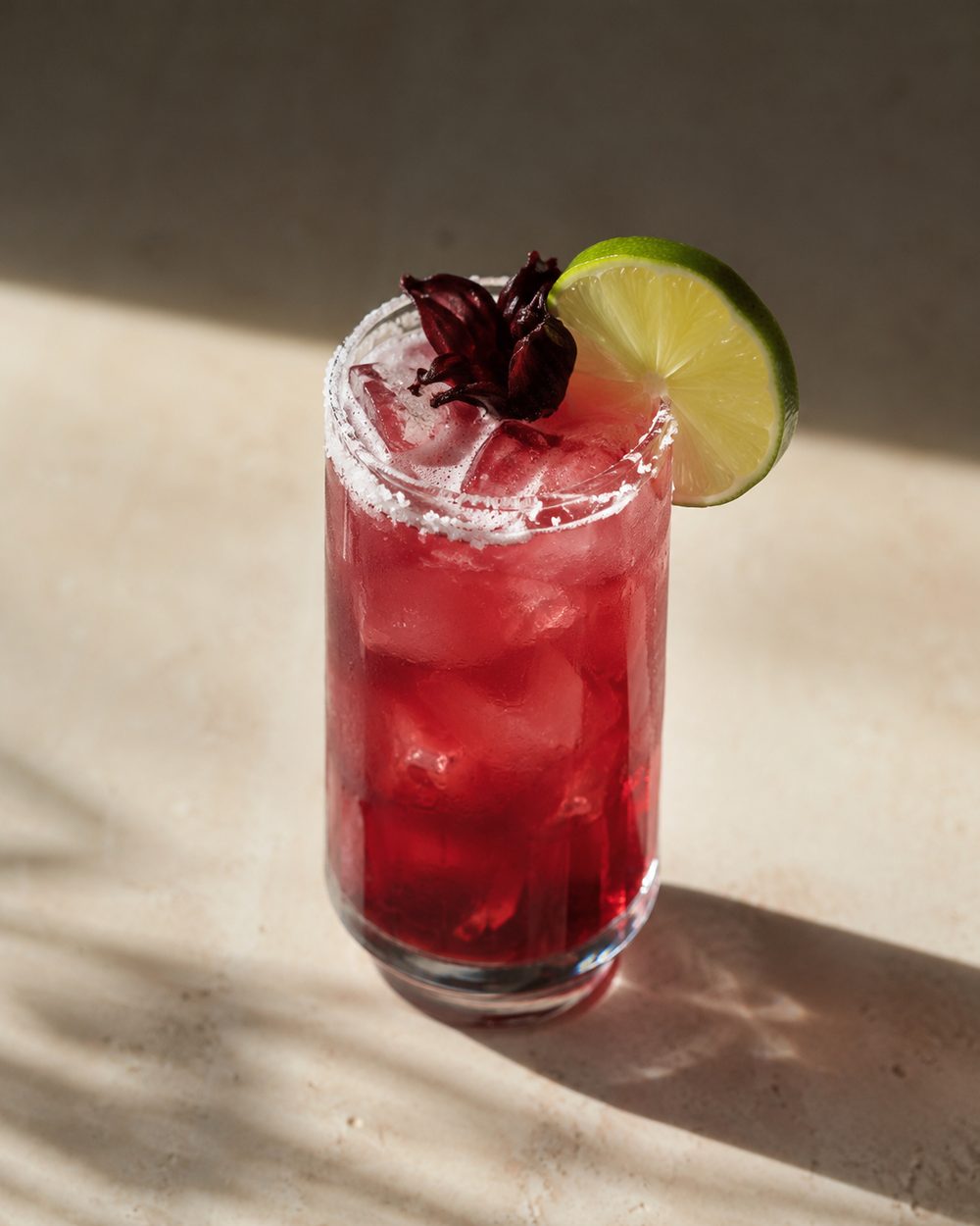 Deep red hibiscus ranch water over ice with a salted rim, lime wheel, and hibiscus flower
